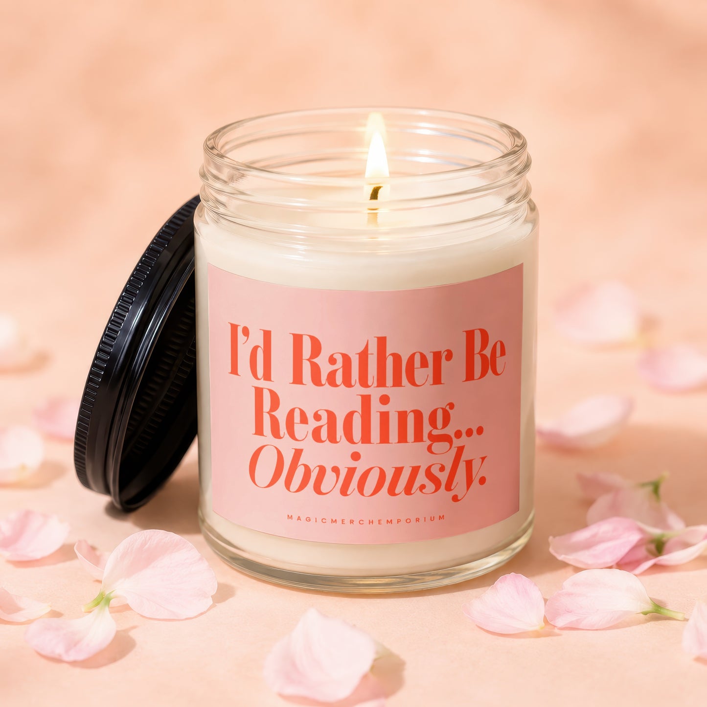 Jar candle with lit wick and pink label reading "I'd Rather Be Reading... Obviously."