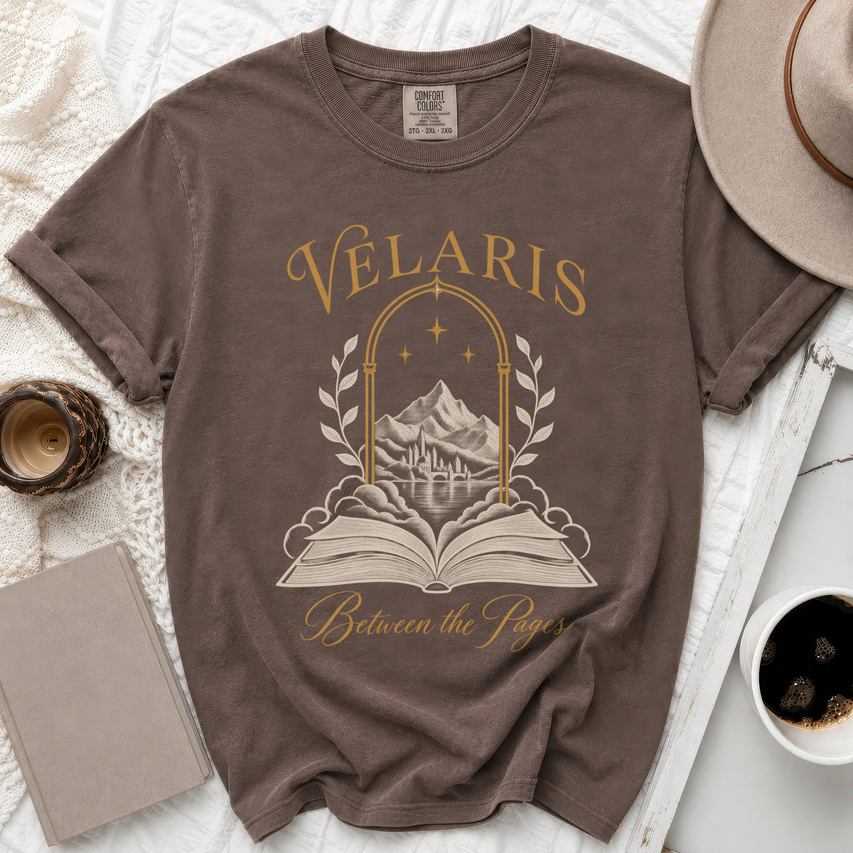 Brown t-shirt with "Velaris Between the Pages" and a scene of mountains and a city through an arch.