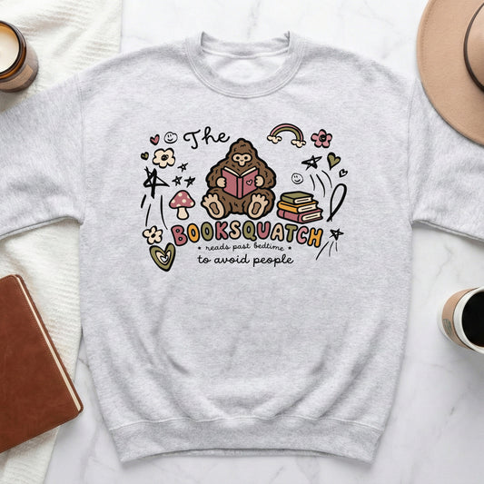 Light grey sweatshirt with a graphic of Bigfoot reading, "The Booksquatch reads past bedtime to avoid people."