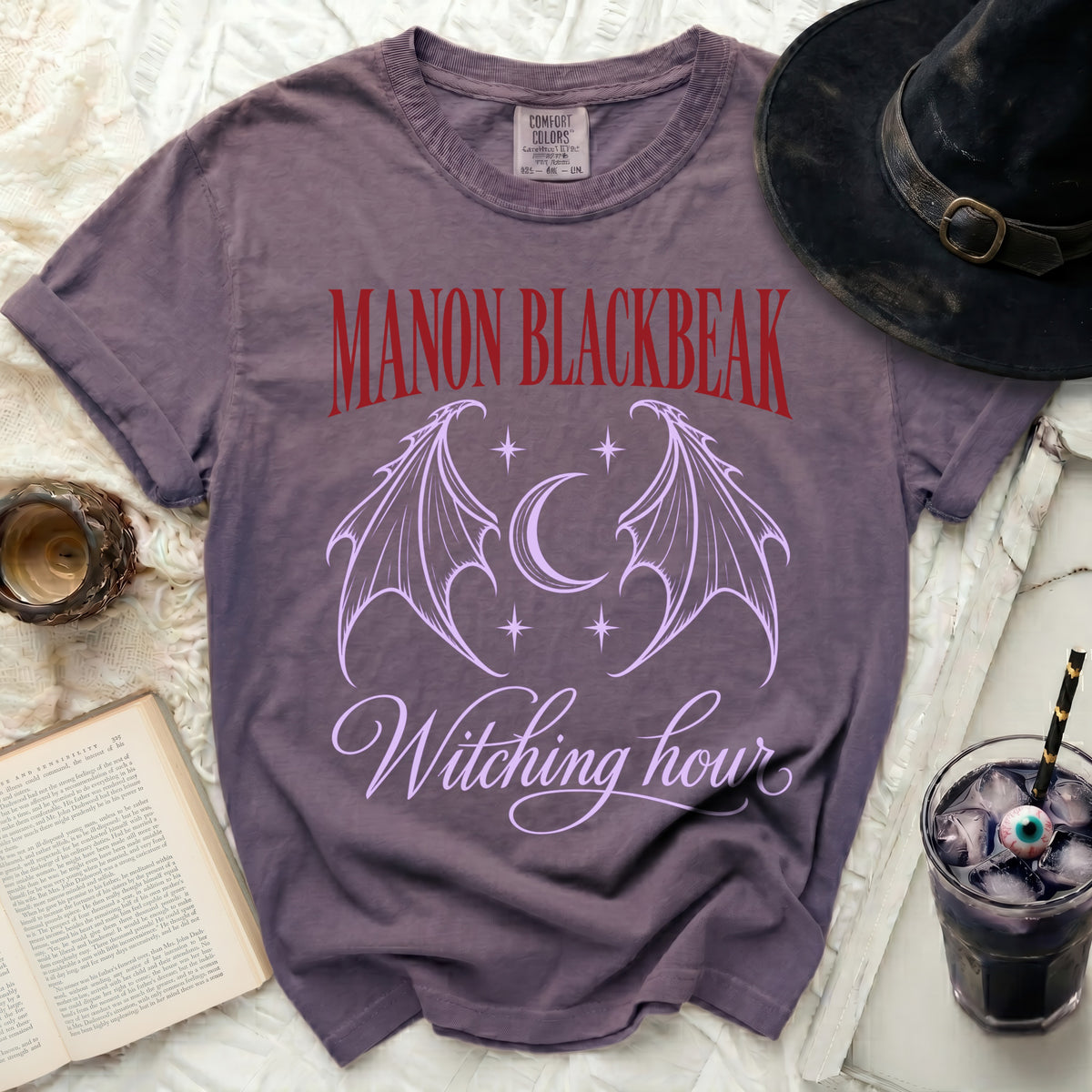 Purple t-shirt with "Manon Blackbeak" and "Witching hour" text and bat wings.