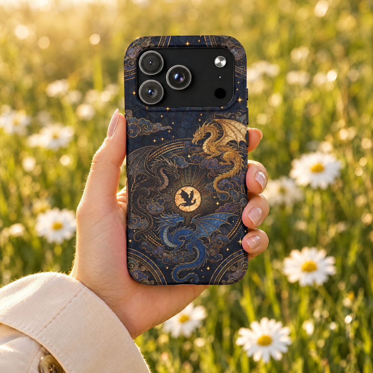 A hand holds a dark blue phone case featuring golden dragons against a blurred daisy meadow background.
