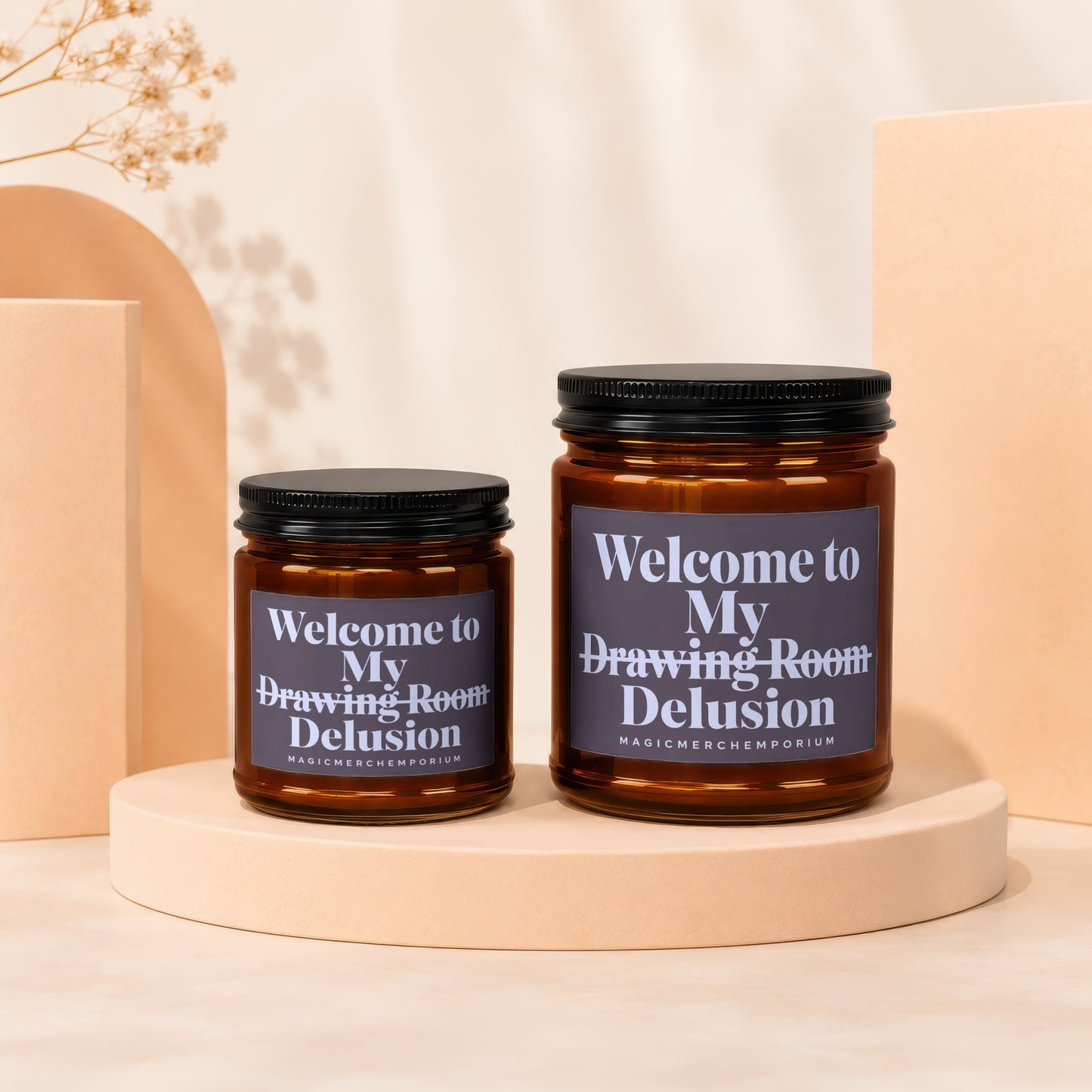 Two brown glass candles with black lids and dark labels reading "Welcome to My Drawing Room Delusion."