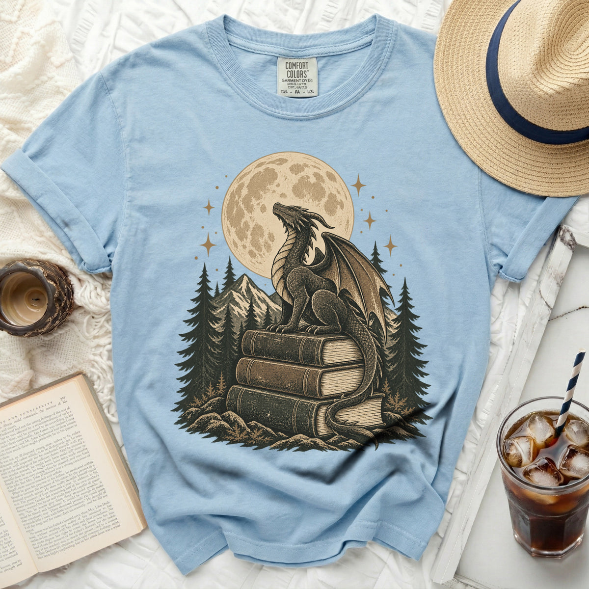 Light blue t-shirt with a dragon sitting on books under a full moon.