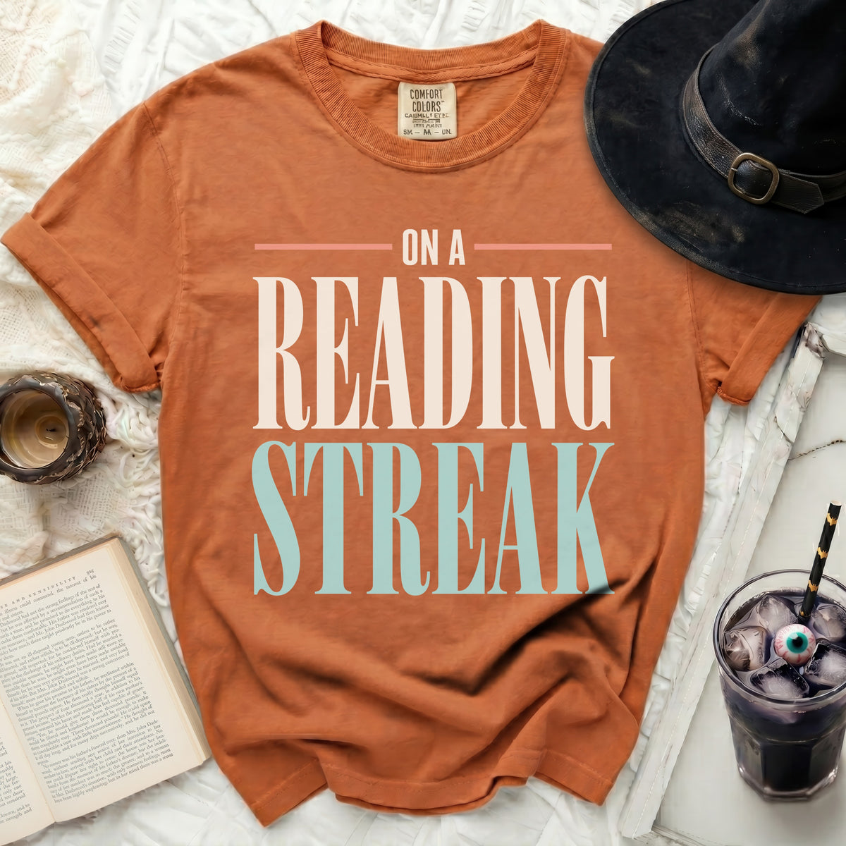 Orange t-shirt with "On a Reading Streak" text, witch hat, book, and spooky drink.