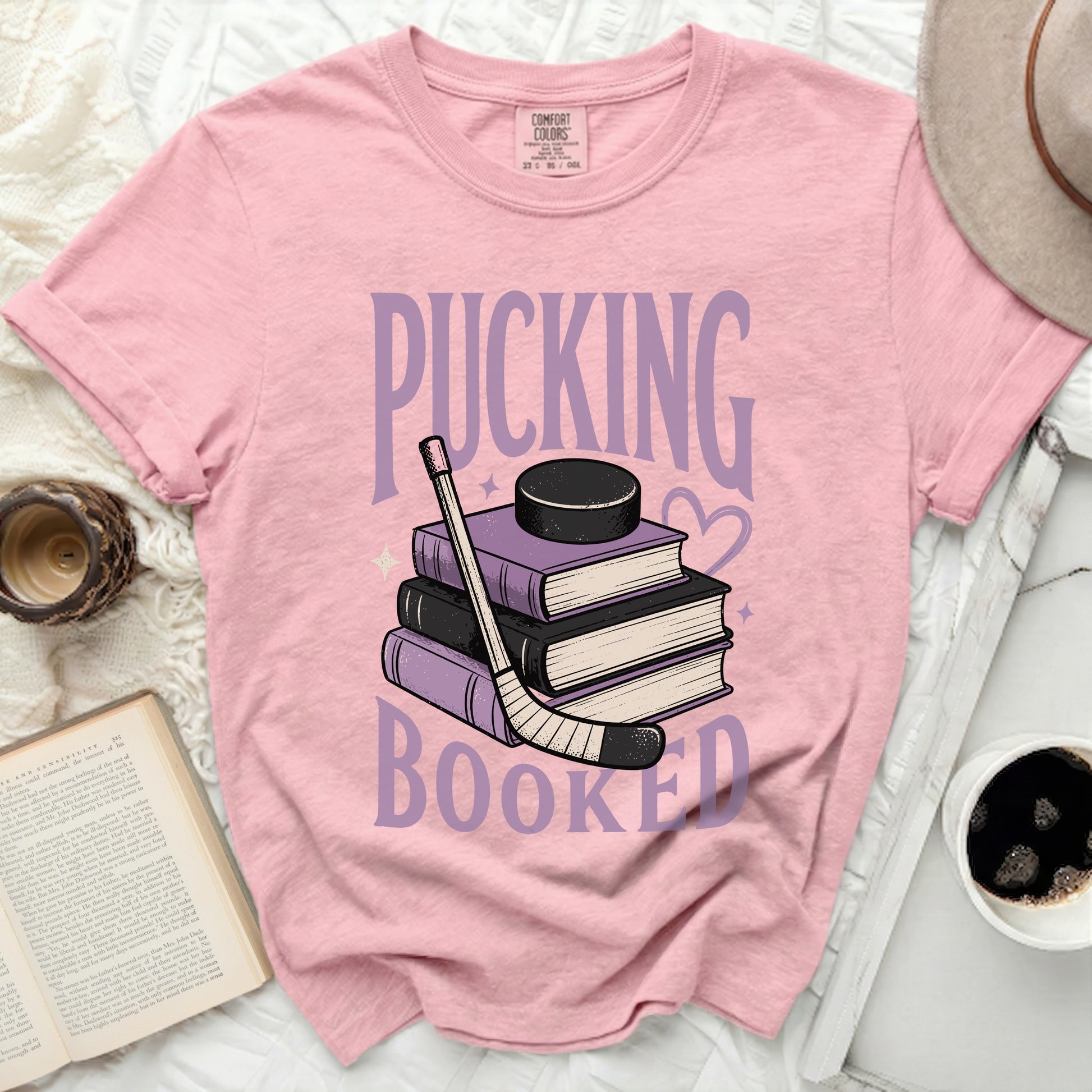 Pink t-shirt with "Pucking Booked" and hockey puck, stick, and books.