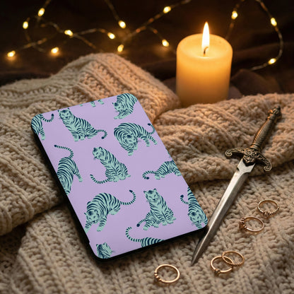 Purple phone case with blue tiger pattern on knitted blanket beside candle and rings.