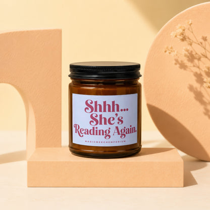 Amber jar candle with white label reading "Shhh... She's Reading Again."