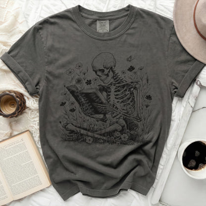 Skeleton reading a book surrounded by flowers and butterflies.