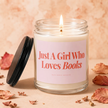 Glass candle with lit wick and pink label reading "Just A Girl Who Loves Books".