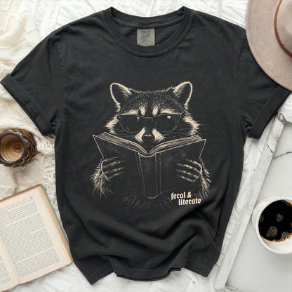 Black t-shirt with raccoon wearing glasses reading a book graphic.