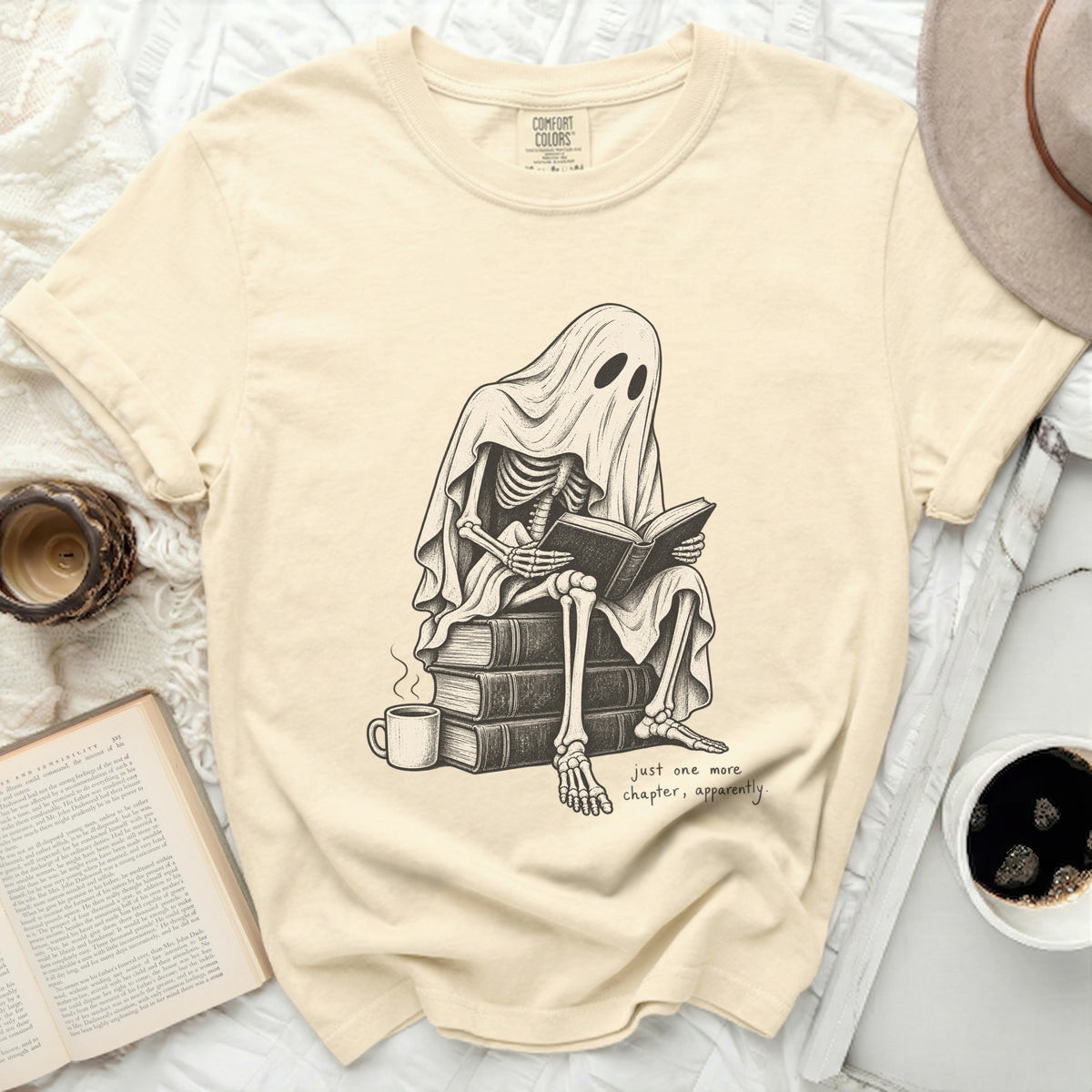 Skeleton under ghost sheet reads book with coffee, "just one more chapter, apparently."