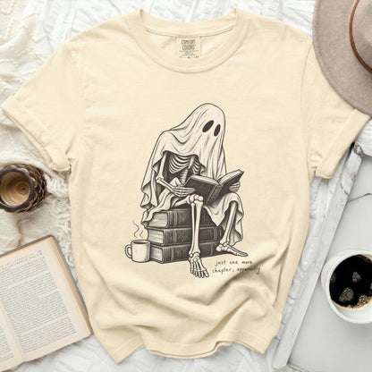 Skeleton under ghost sheet reads book with coffee, "just one more chapter, apparently."