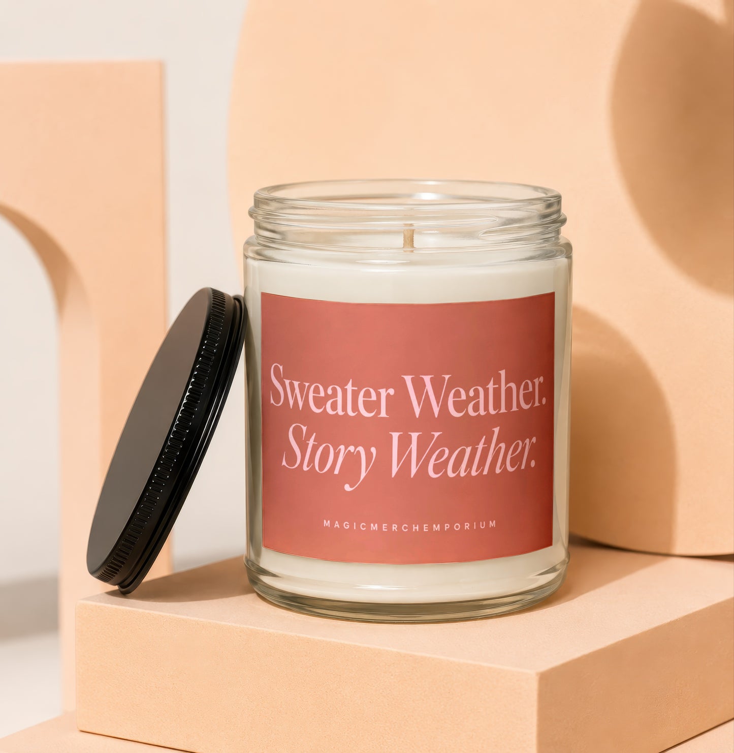 Glass candle with pink label reading "Sweater Weather. Story Weather."