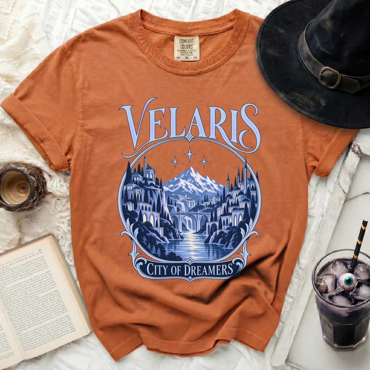 Orange t-shirt with "Velaris City of Dreamers" fantasy landscape print.