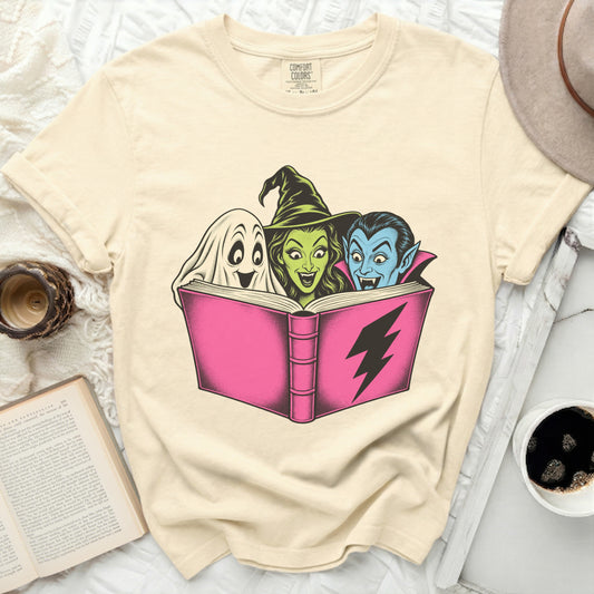 Ghost, witch, and vampire reading a pink book with a lightning bolt.