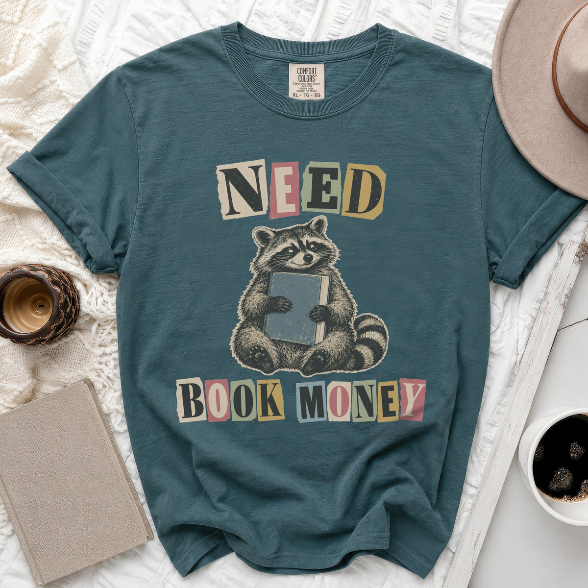 Teal t-shirt with raccoon graphic and text "NEED BOOK MONEY"