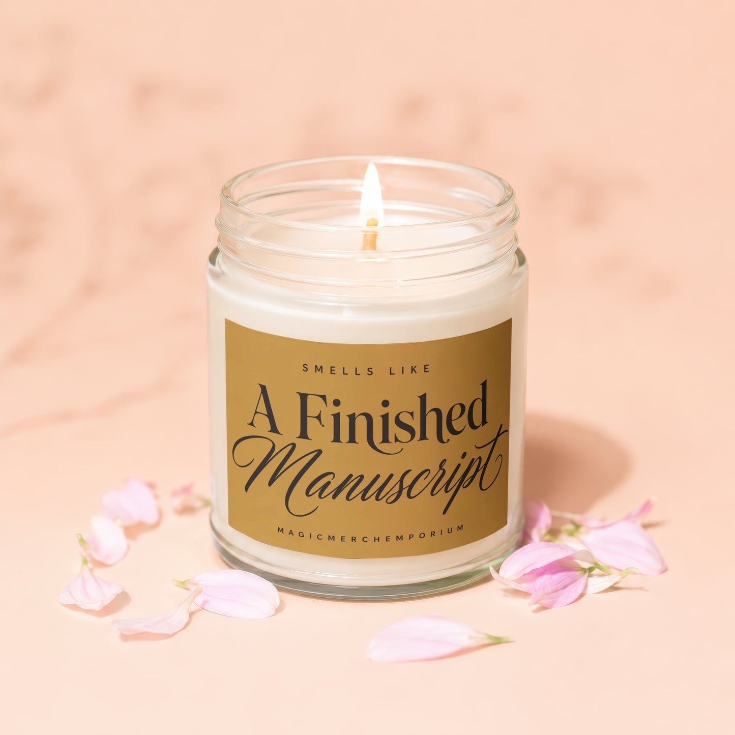 Lit candle in a glass jar with gold label reading "Smells Like A Finished Manuscript".
