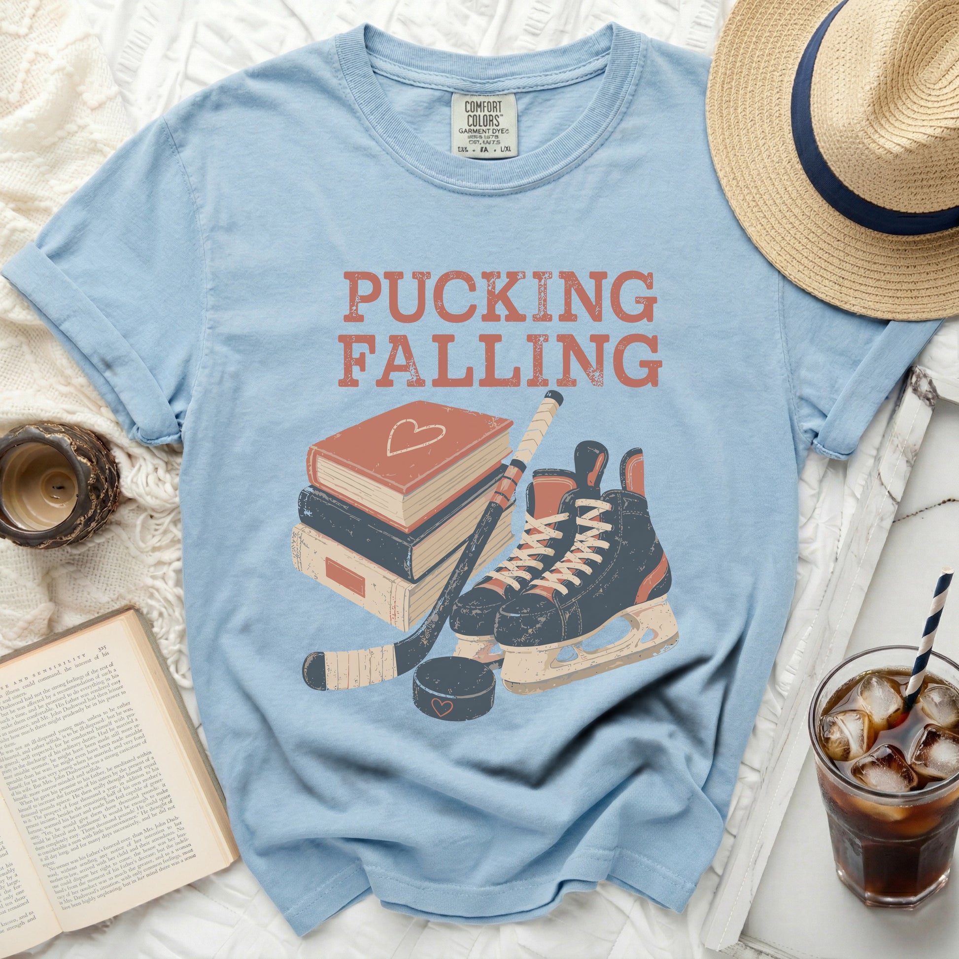 Light blue t-shirt with "PUCKING FALLING" text, hockey skates, stick, and books.
