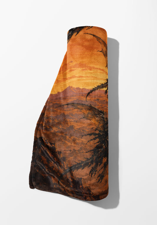Rolled blanket with desert landscape and palm tree silhouette in sunset tones.