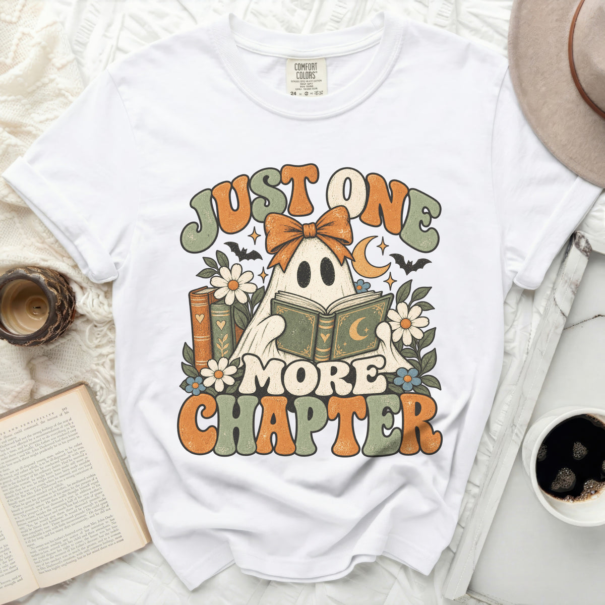 White t-shirt with graphic that says "Just One More Chapter" and a ghost reading.