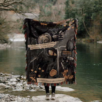 A person is standing on a rock, holding a large blanket with various images and text printed on it, including a dragon, stars, and a quote.