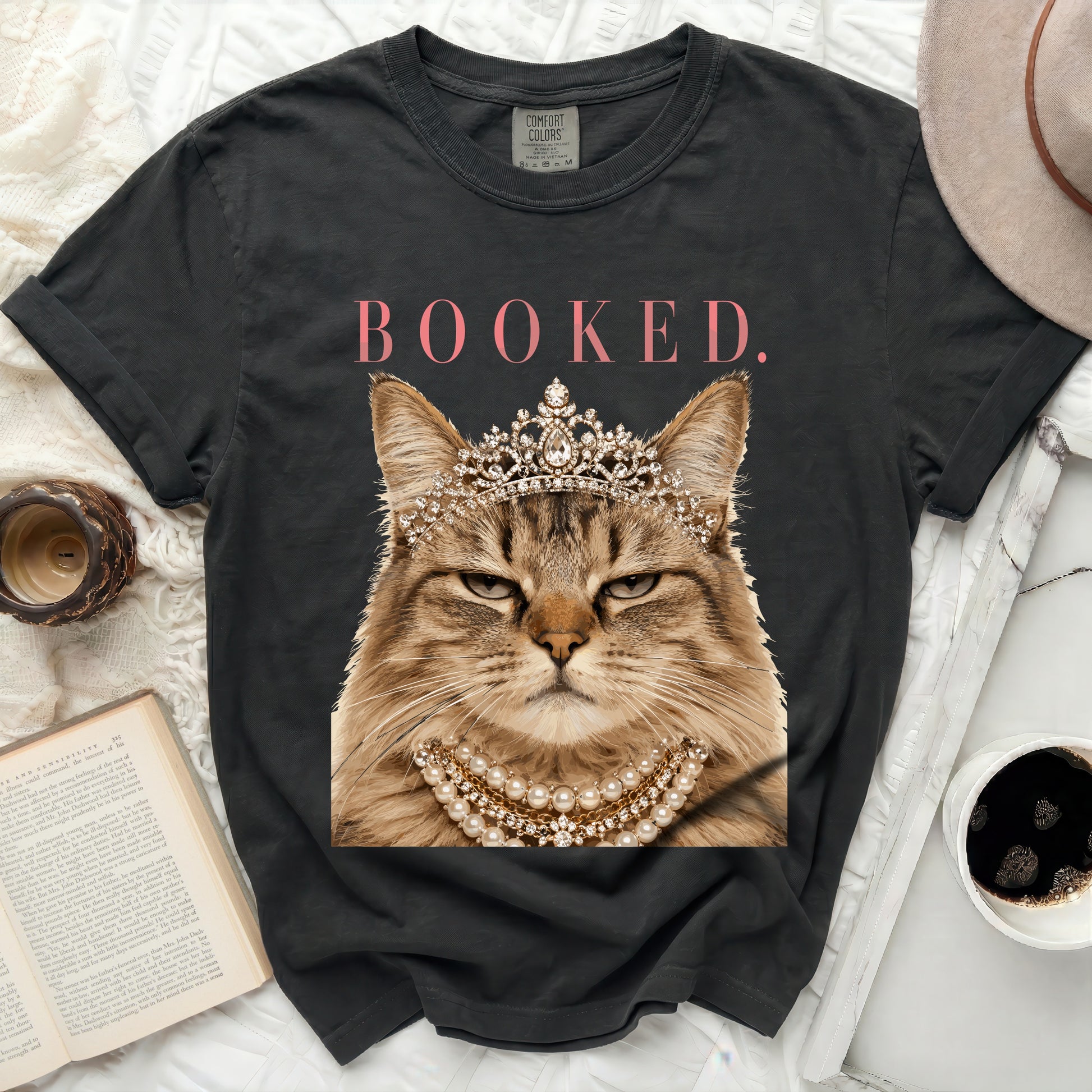 Black t-shirt with a cat wearing a crown and pearls, text "BOOKED."