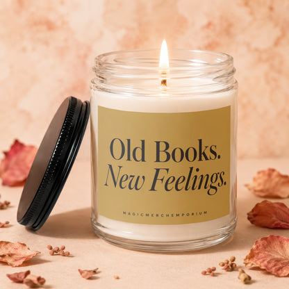 Lit candle with gold label reading "Old Books. New Feelings." and "MAGICMERCH"}, surrounded by dried leaves.