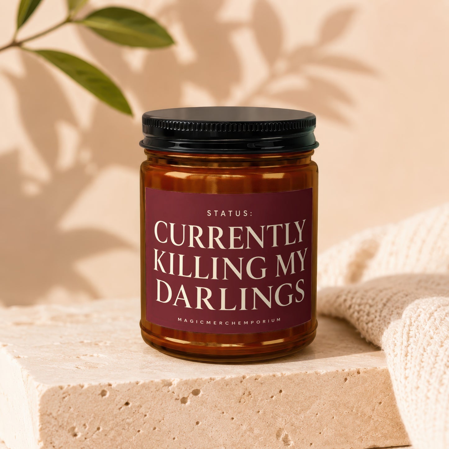 Amber jar candle with black lid reading "STATUS: CURRENTLY KILLING MY DARLINGS".