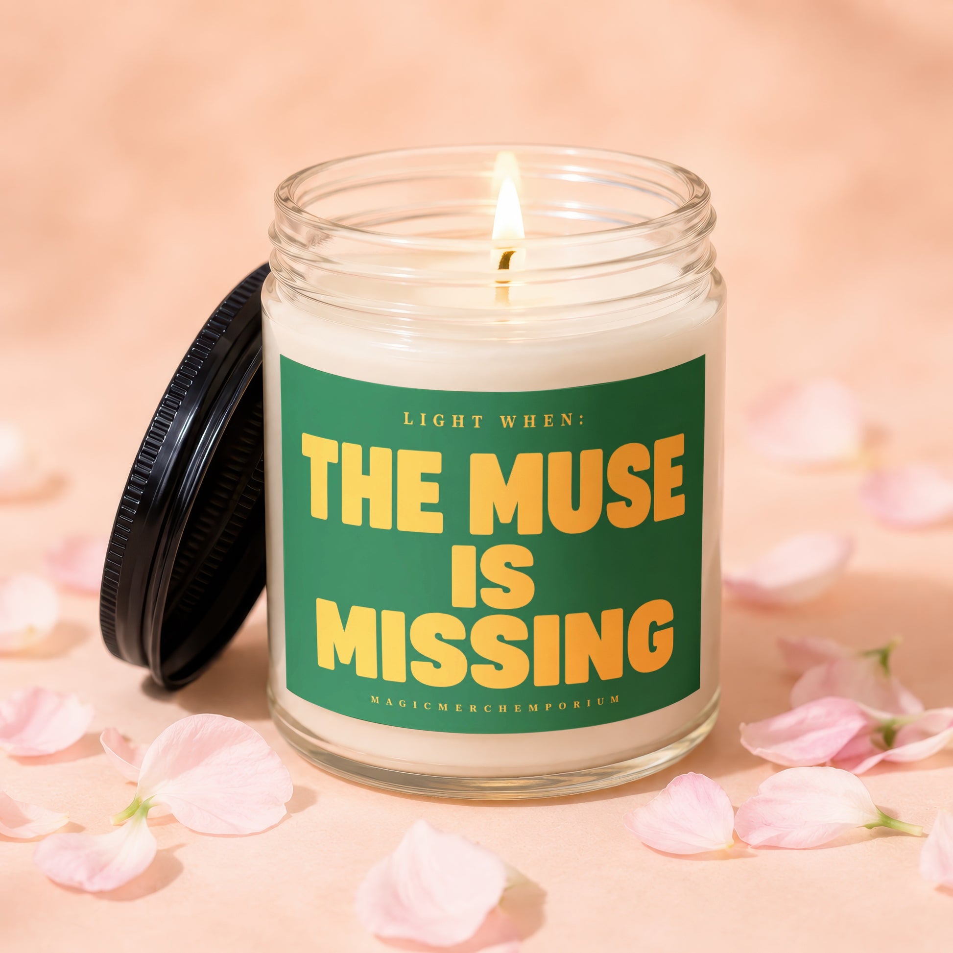 Lit candle in a glass jar with a green label that reads "THE MUSE IS MISSING".