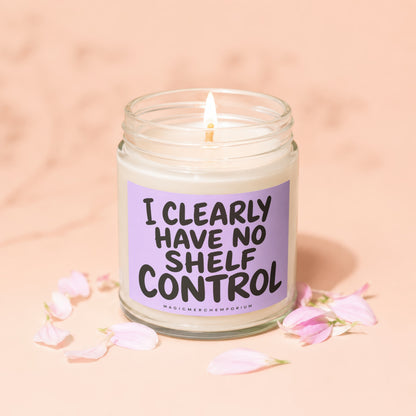 Glass jar candle with lit wick, reads "I clearly have no shelf control"