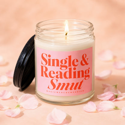 Glass candle with lit wick and "Single & Reading Smut" text on pink label.