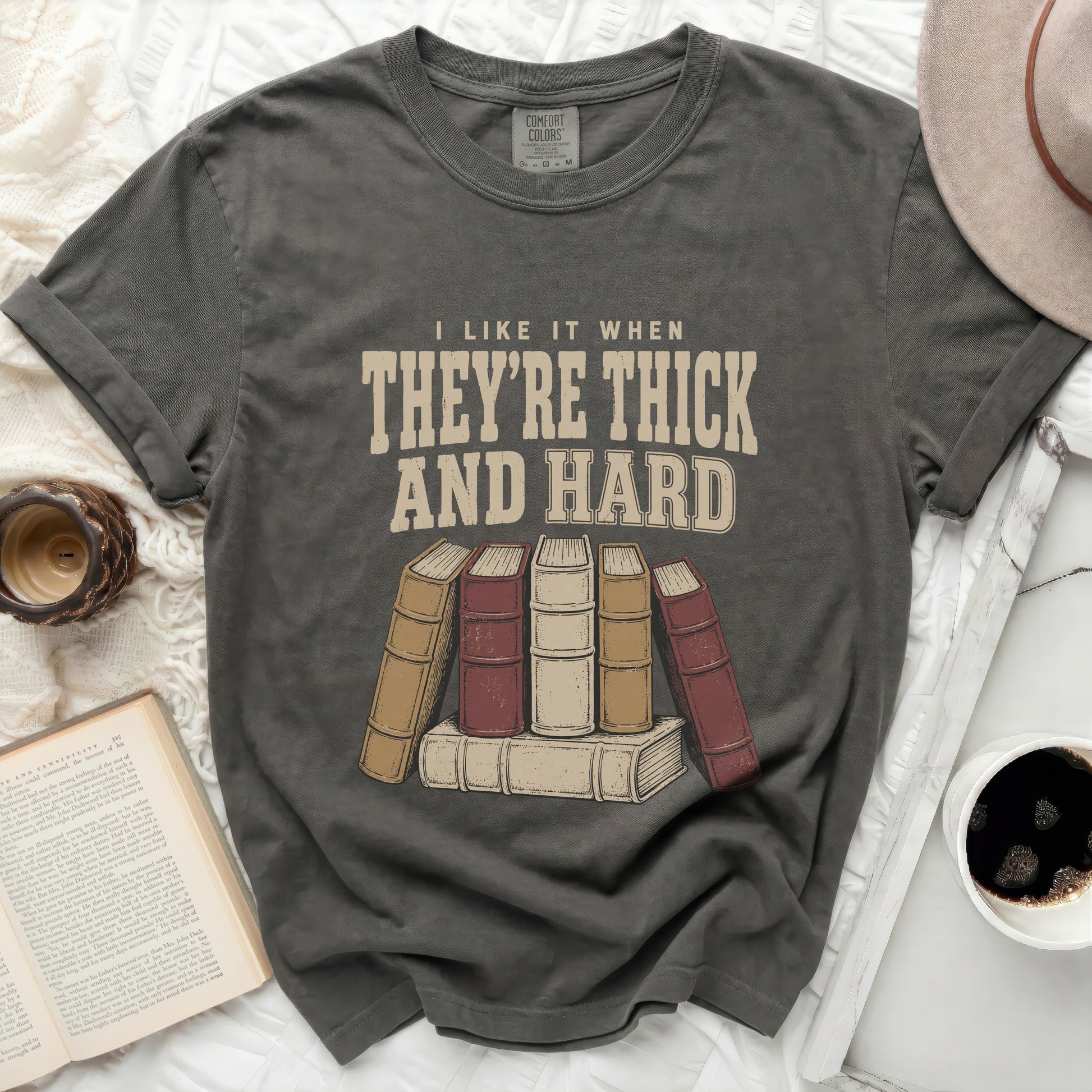 Graphic tee with text "I LIKE IT WHEN THEY'RE THICK AND HARD" above books.