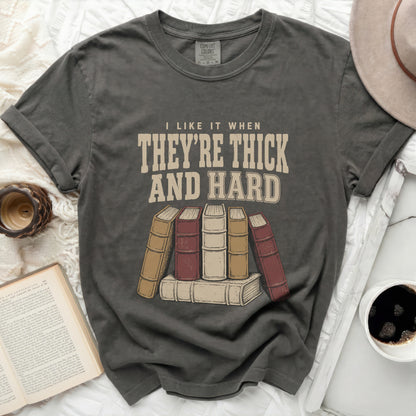 Graphic tee with text "I LIKE IT WHEN THEY'RE THICK AND HARD" above books.