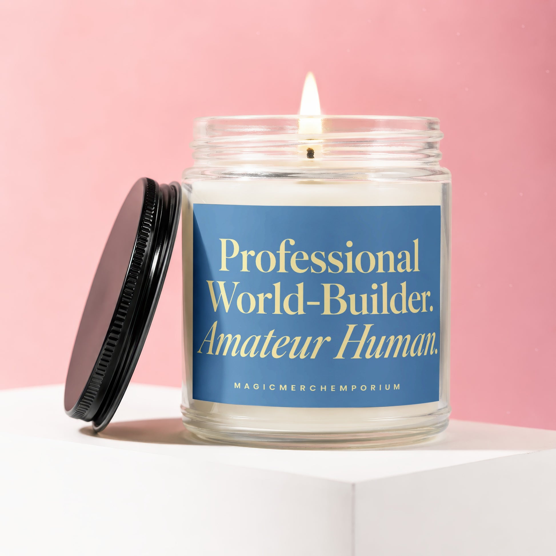 Candle with blue label reading "Professional World-Builder. Amateur Human. MAGICMERCH.COM"
