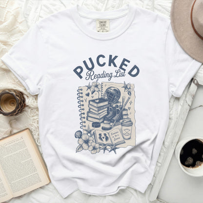 White t-shirt with "Pucked Reading List" graphic featuring books, hockey gear, and flowers.