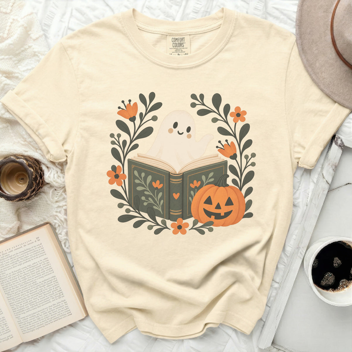 Cream t-shirt with a graphic of a ghost reading a book with a pumpkin and flowers.
