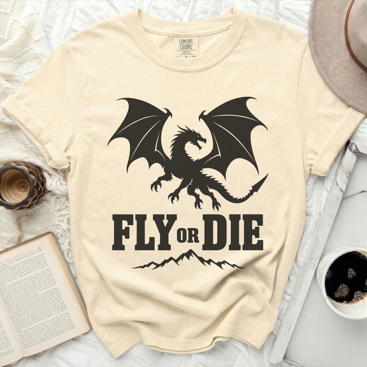 Cream-colored t-shirt with a black graphic of a winged dragon, mountains, and the text FLY OR DIE.