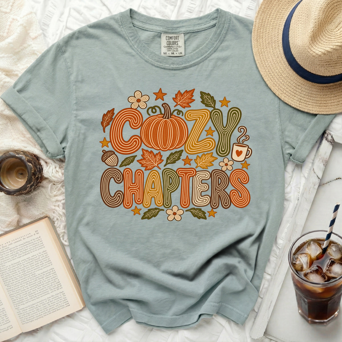 Dusty blue t-shirt with "Cozy Chapters" graphic featuring a pumpkin and autumn leaves.
