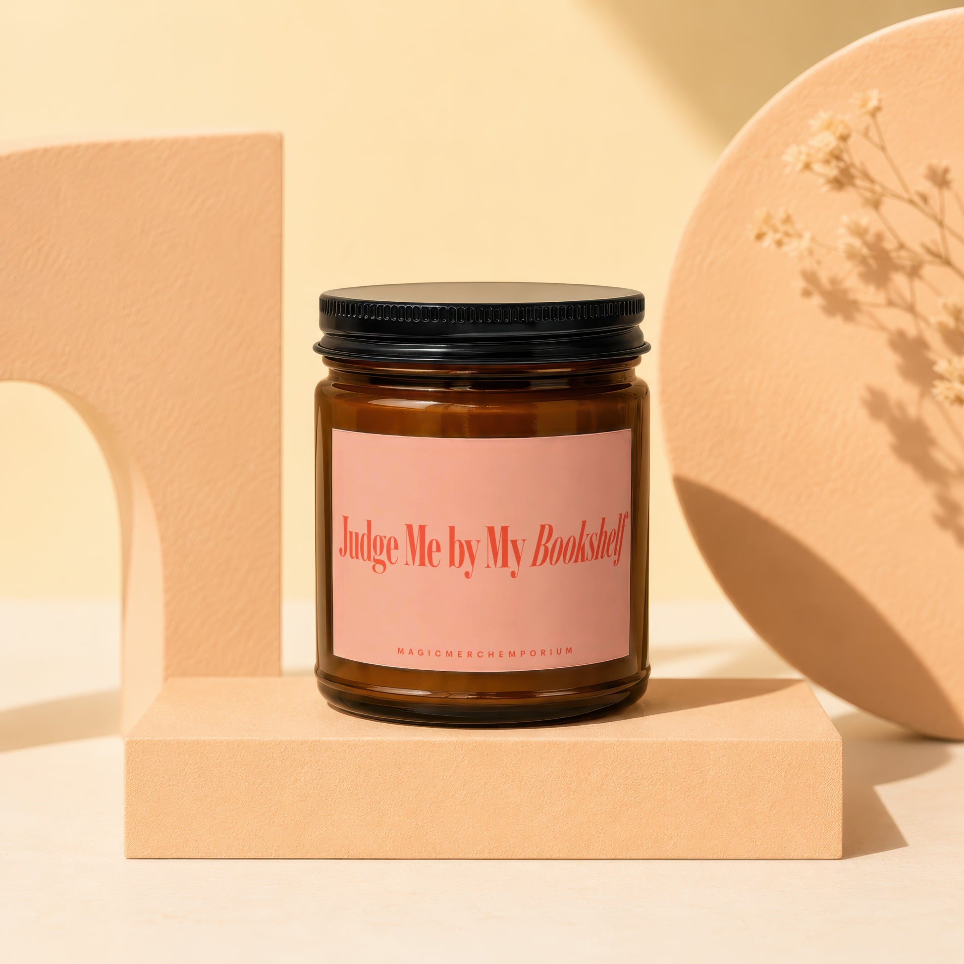 Amber glass candle with pink label reading "Judge Me by My Bookshelf".