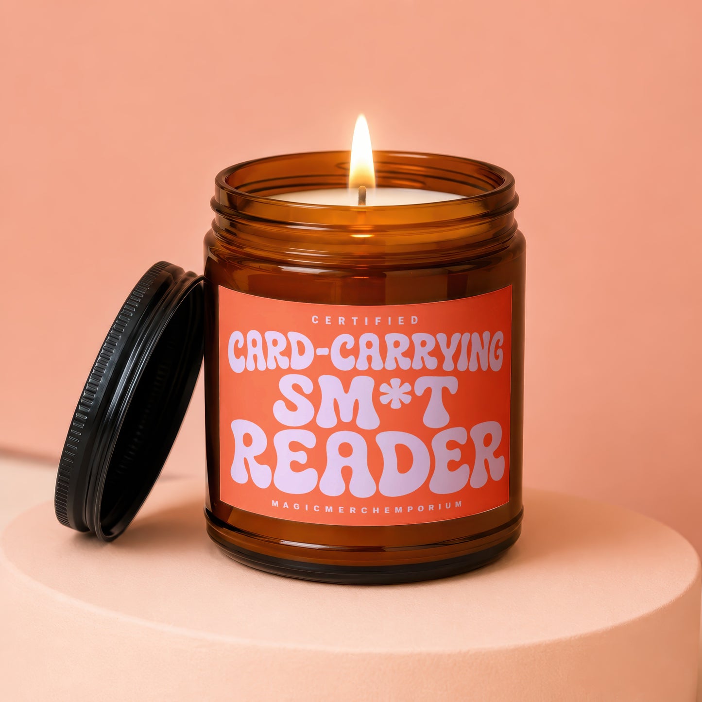 Amber jar candle with orange label reading "CERTIFIED CARD-CARRYING SM*T READER".
