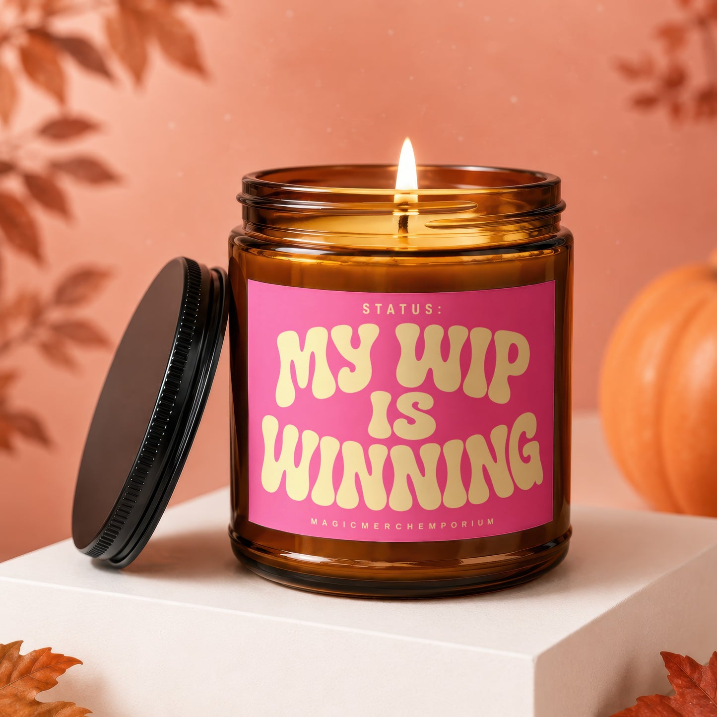 Lit amber candle in jar with pink label reading "Status: My WIP is Winning."