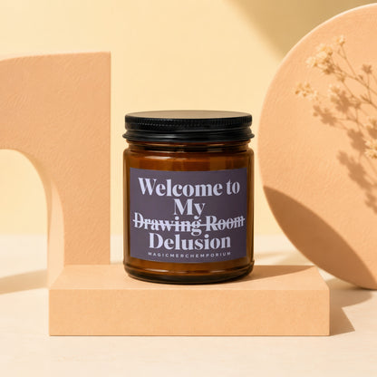 Amber glass candle with black lid titled "Welcome to My Drawing Room Delusion."