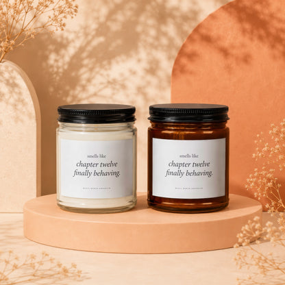 Two candles with black lids on a peach-colored platform, text reads "smells like chapter twelve finally behaving."