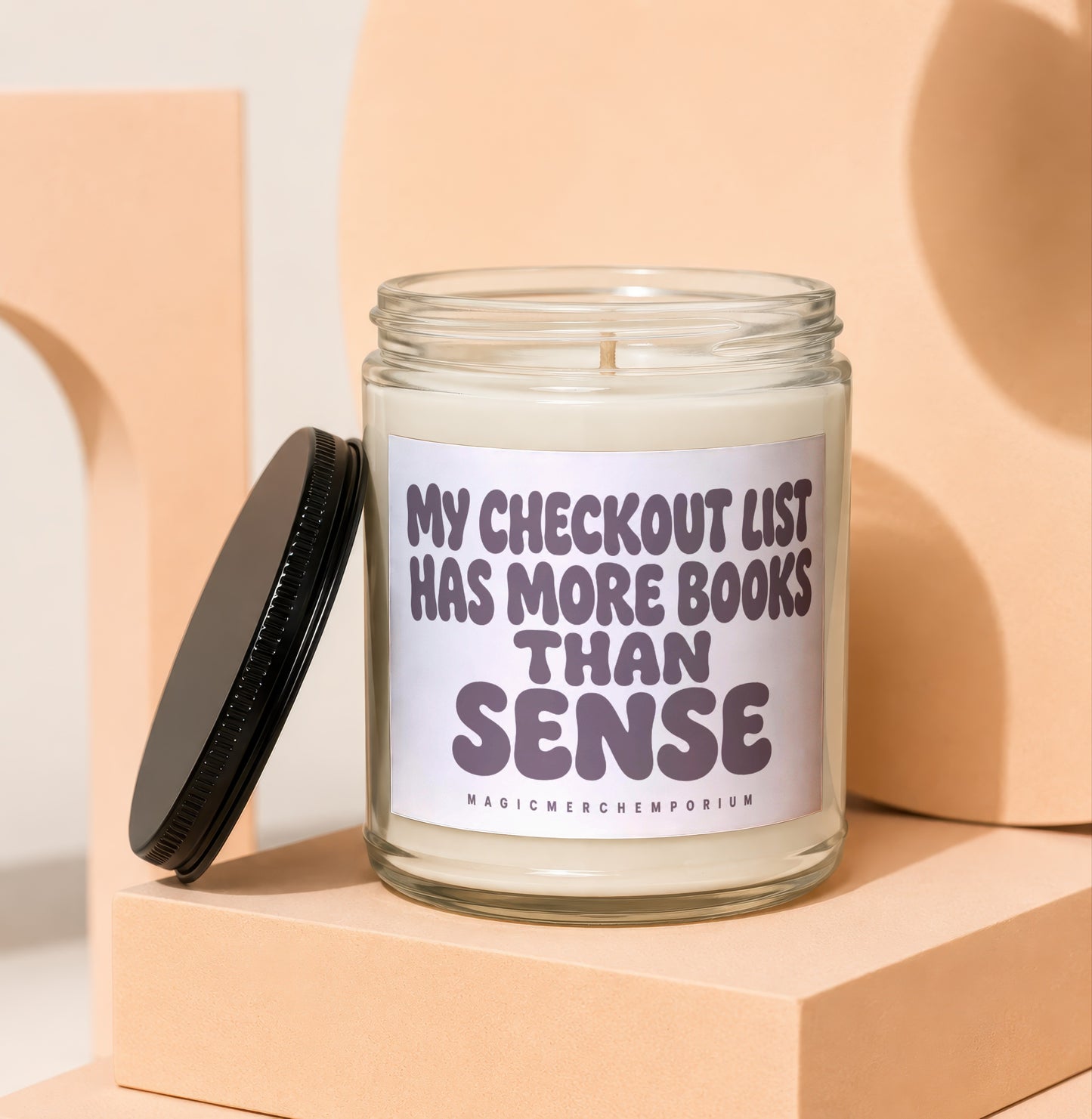 Candle in glass jar with lid off, reading "My checkout list has more books than sense".