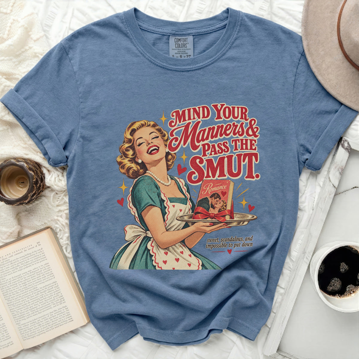 Blue t-shirt with vintage illustration of woman holding romance book, text "MIND YOUR Manners & PASS THE SMUT".