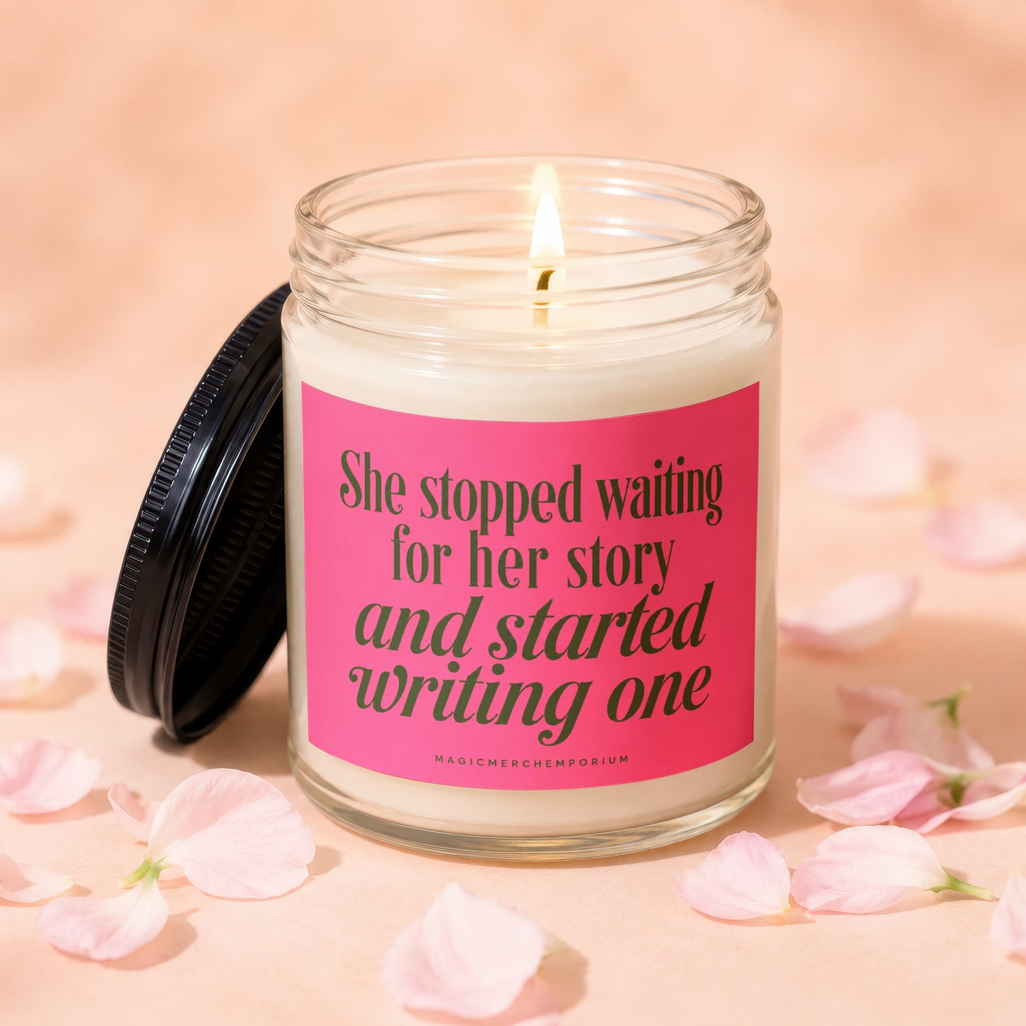 Glass candle with lit wick and pink label reading "She stopped waiting for her story and started writing one."