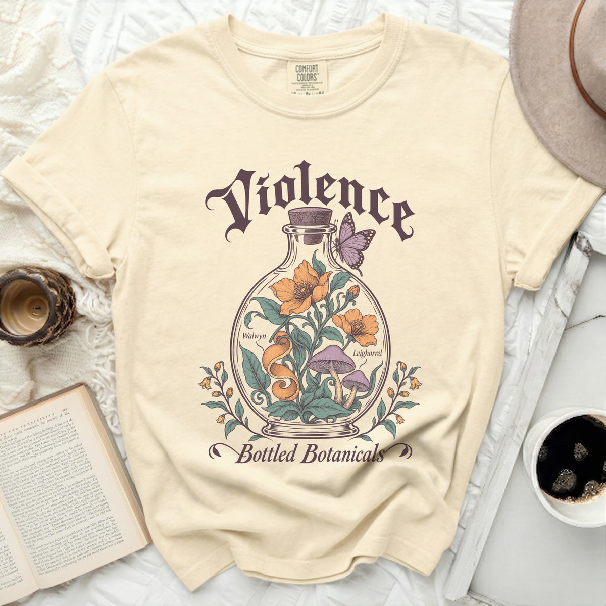 A cream-colored t-shirt with a vintage graphic of a glass bottle containing flowers, mushrooms, and text.