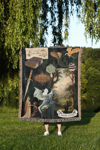 A person is standing in a grassy area, holding a large tapestry or blanket that features a dragon, a book, and other fantastical elements.