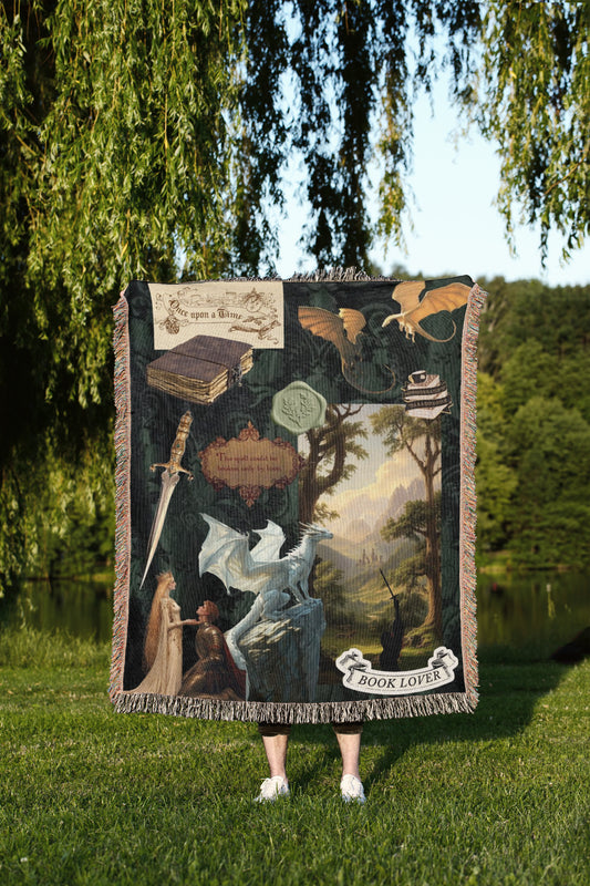 A person is standing in a grassy area, holding a large tapestry or blanket that features a dragon, a book, and other fantastical elements.