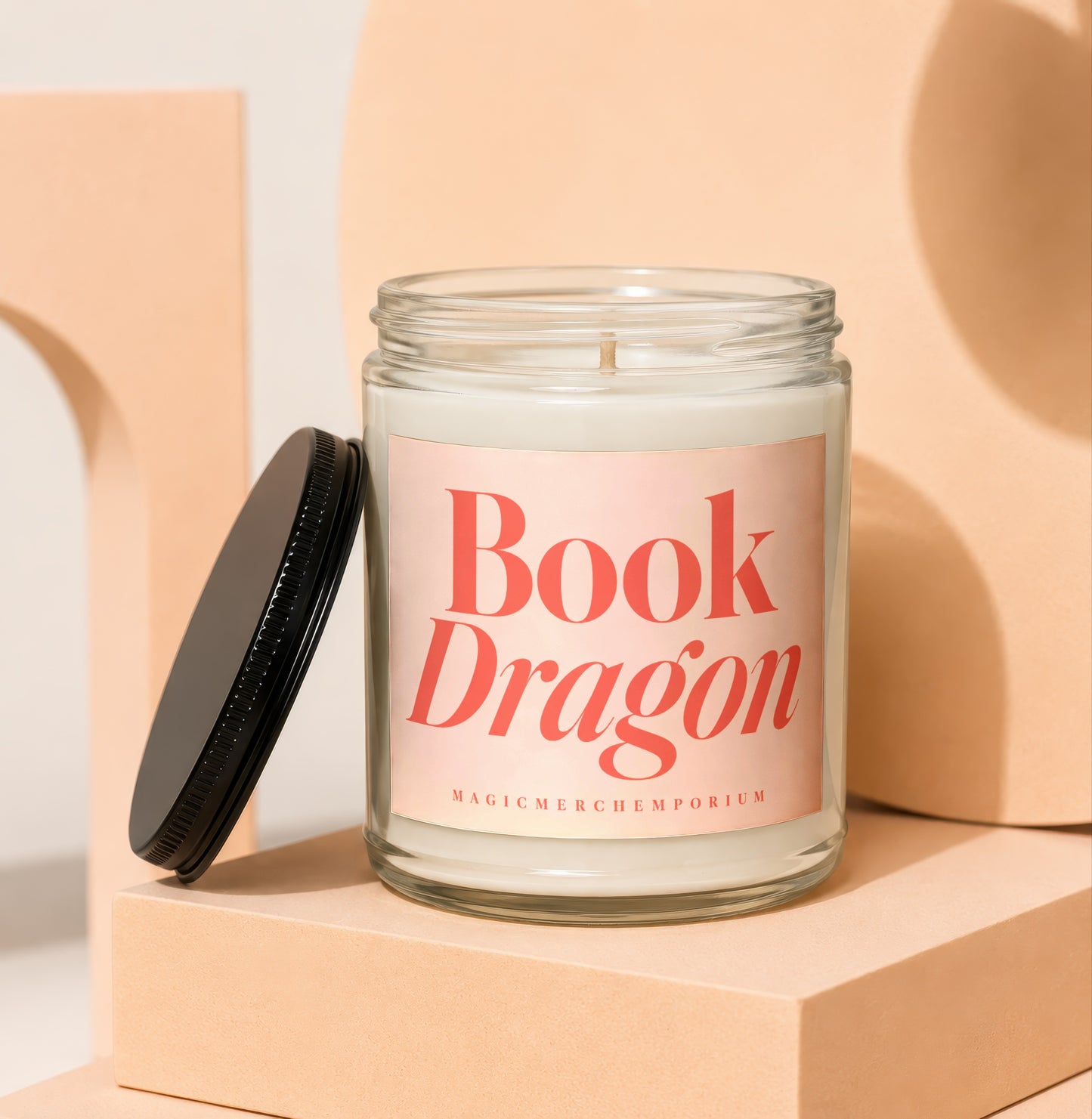 Glass candle with "Book Dragon" and "MagicMerchEmporium" text on a light pink label.